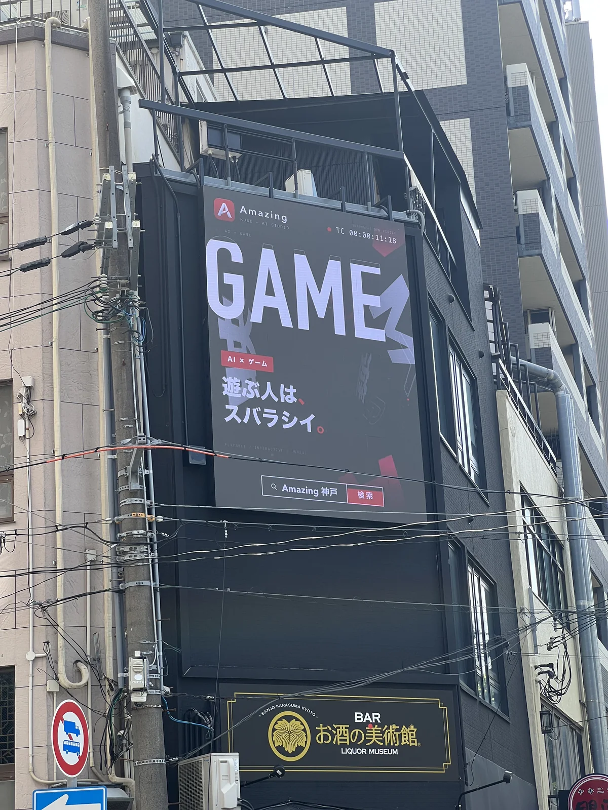歩道から見上げたビジョンとビル。「GAME 遊ぶ人は、スバラシイ。」のカットが映っている